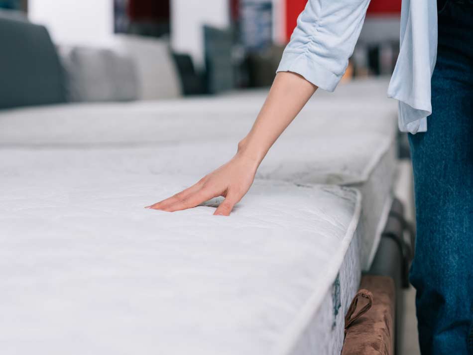 Customer feeling mattress, like those available in Lubbock at Rustic Furniture Warehouse.